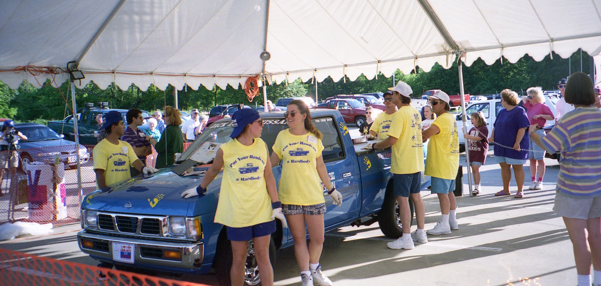 Contestants in yellow contest shirts with their hands on the blue pickup under the white tent