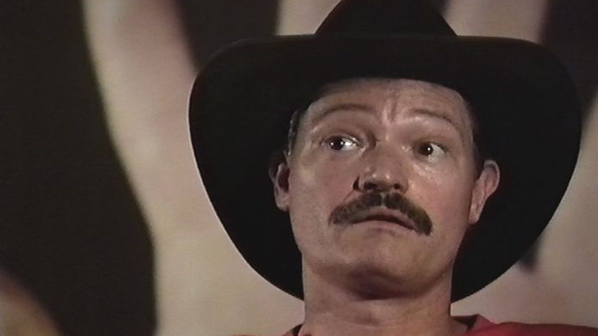 Benny, in a black cowboy hat, with a hand raised behind him